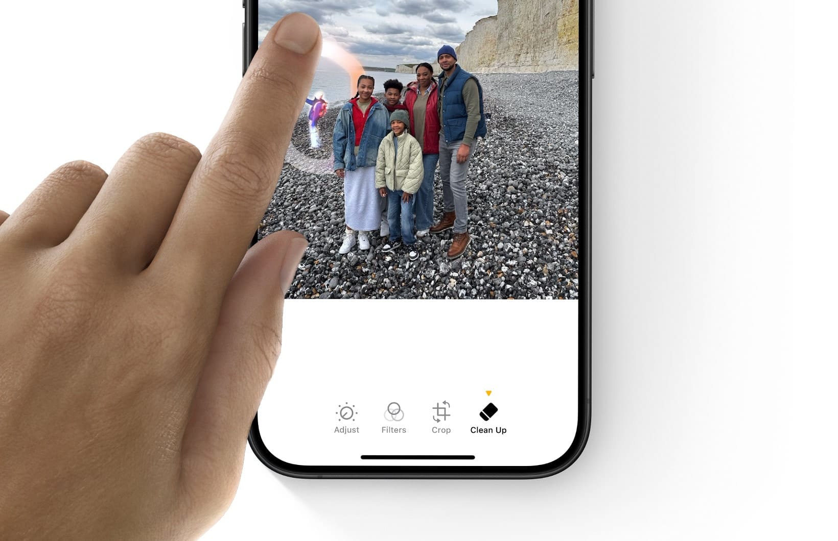 A finger using the Clean Up tool in Photos to erase a distraction from a family photograph taken on a pebble beach