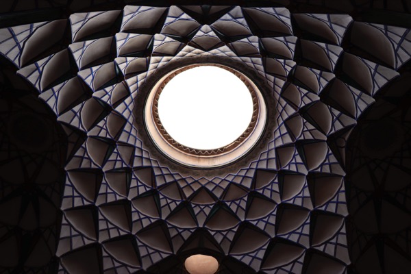 Looking up at an ornate tiled dome with a bright circular opening at its center