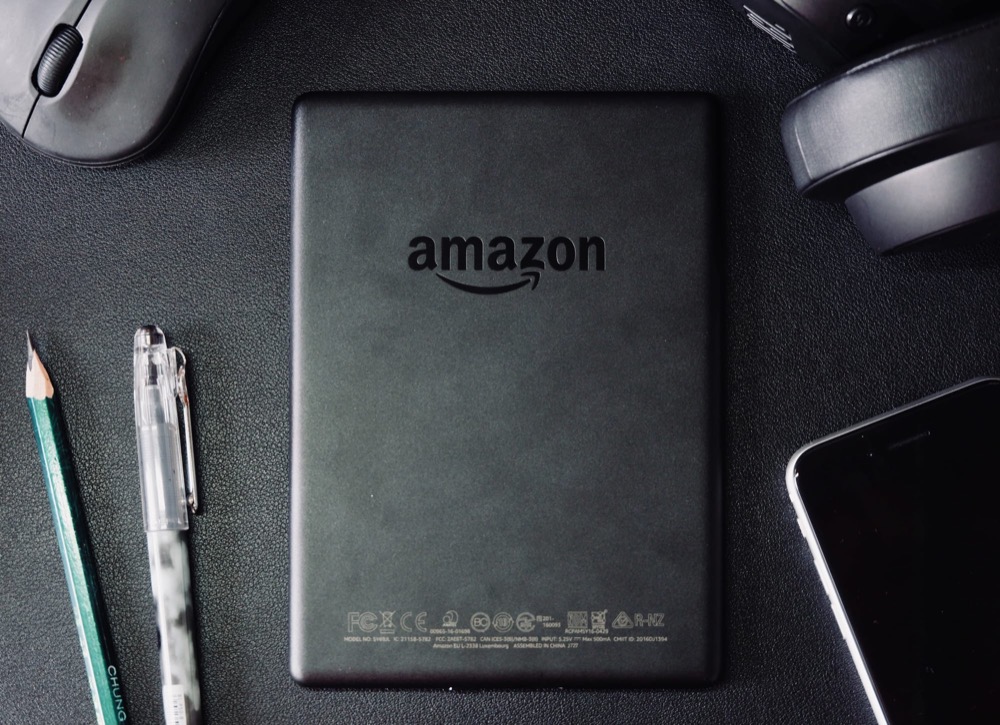 An Amazon e-reader on a desk beside a pencil, headphones and a mouse