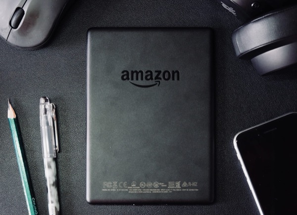 An Amazon e-reader on a desk beside a pencil, headphones and a mouse