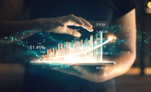 Hands held over a tablet, with a glowing bar chart and figures rising above the screen