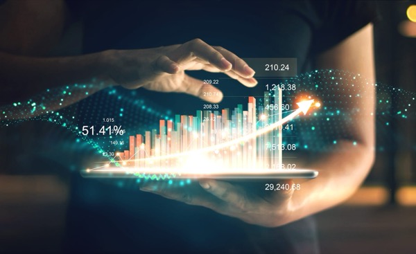 Hands held over a tablet, with a glowing bar chart and figures rising above the screen