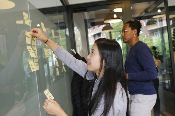 Three people arranging sticky notes on a glass wall