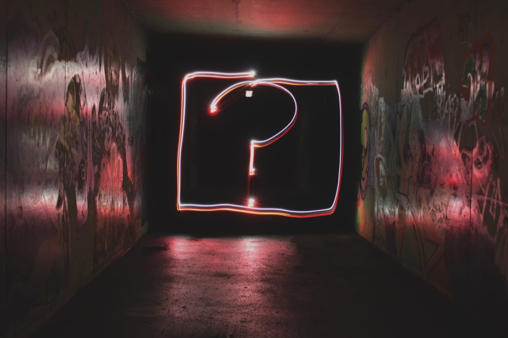 A neon question mark glowing at the end of a dark, graffiti-covered tunnel