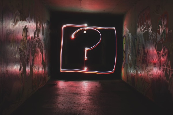 A neon question mark glowing at the end of a dark, graffiti-covered tunnel