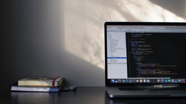 A laptop showing code on a desk beside a small stack of books, in low afternoon light
