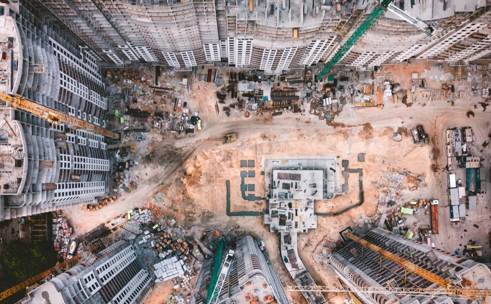 An aerial view of a large construction site, with cranes standing around exposed foundations