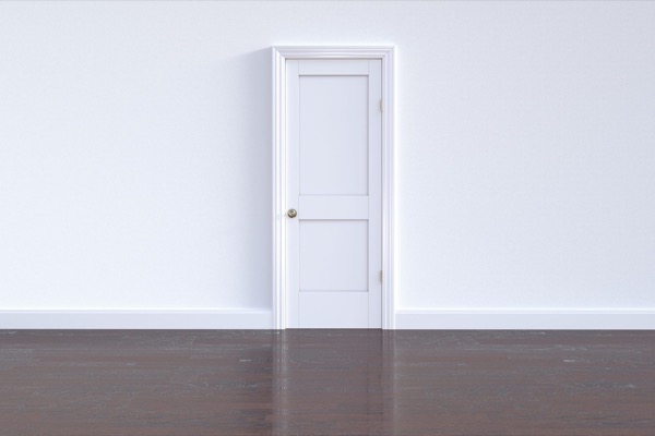 A single closed white door in an empty white room with a dark wood floor