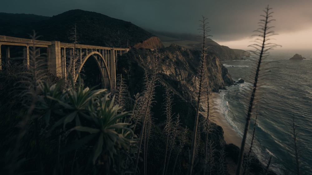 A concrete arch bridge spanning a cliff above a dark, stormy coastline