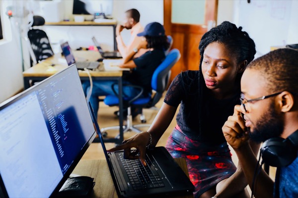 Two colleagues looking together at code on a laptop screen in an open office