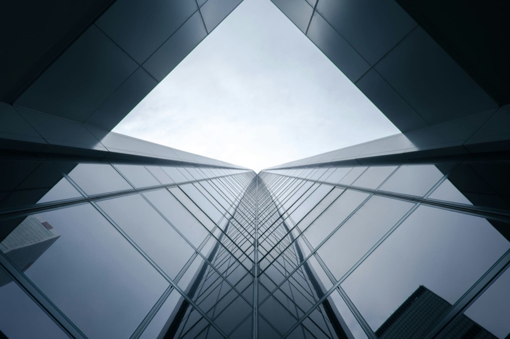 Looking straight up between glass office towers converging against a pale sky