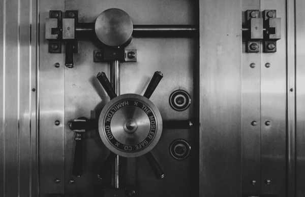A bank vault door with a large combination dial, in black and white