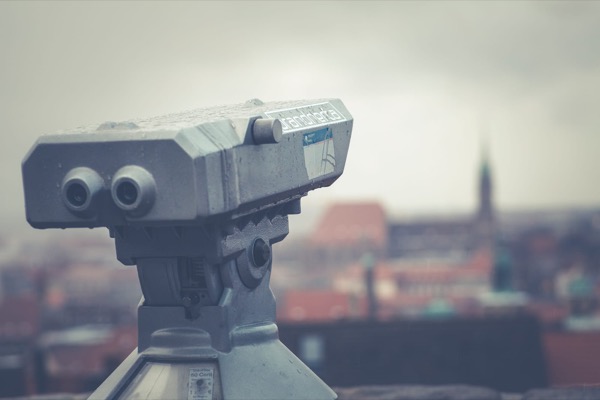 A coin-operated viewing telescope on a terrace above a hazy city skyline
