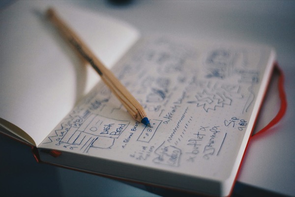 An open notebook of hand-drawn interface sketches, with a pencil resting on the page